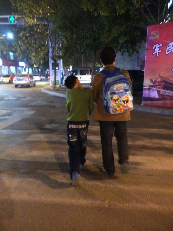 一位父亲接下辅导班放学回家的孩子,背着儿子的书包.