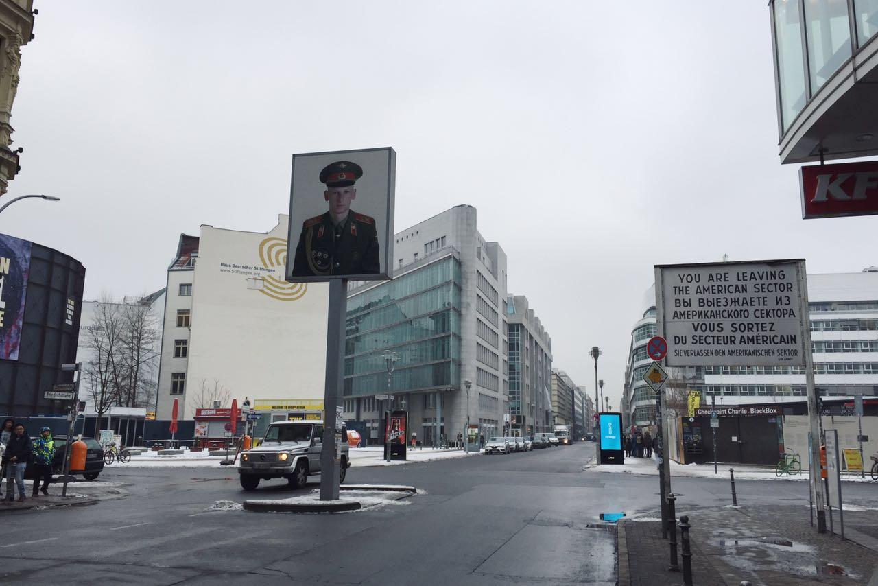 检查哨前方有一个立牌,面向东柏林的一面贴有苏联红军的士兵照片,西