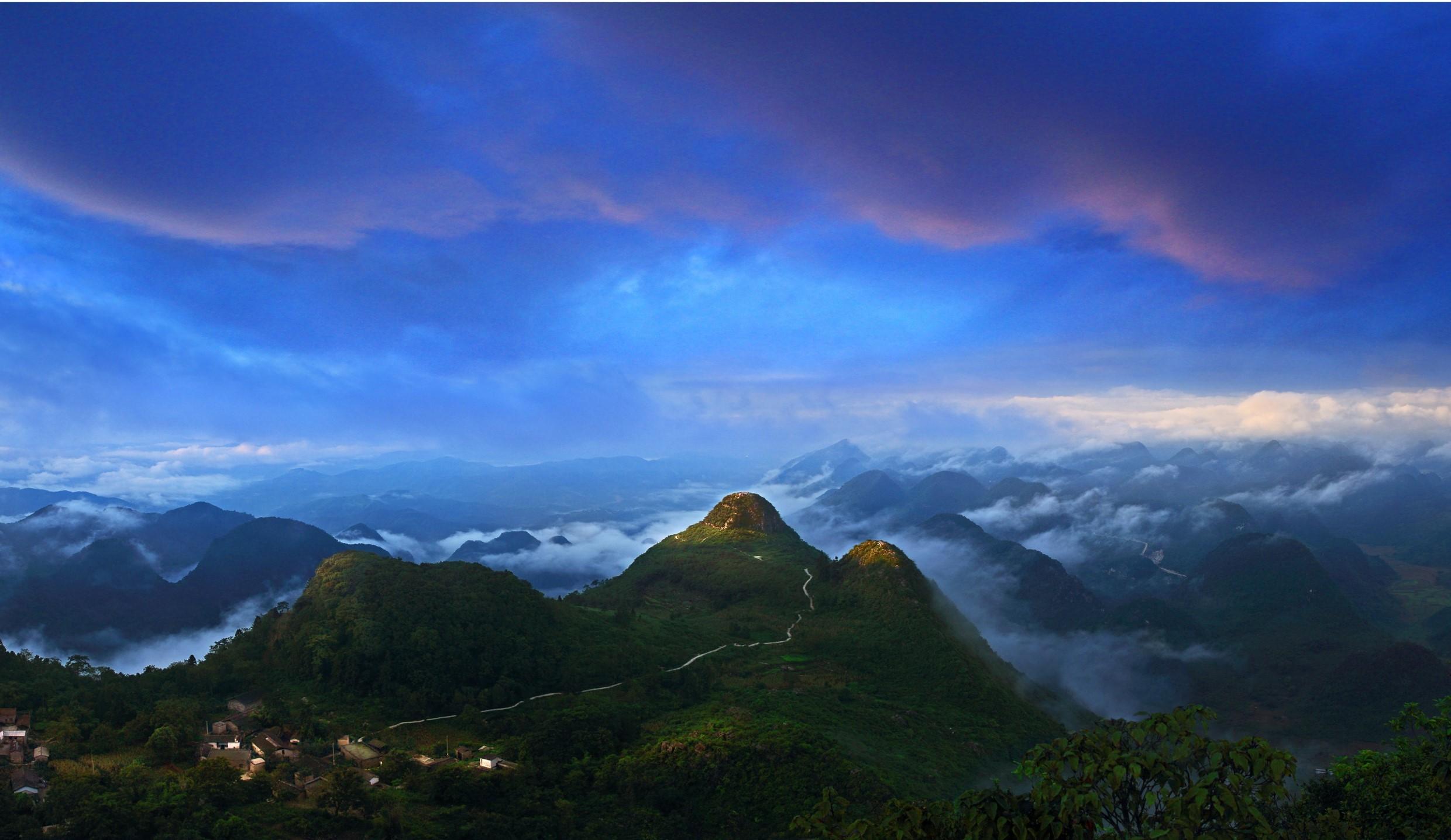 在版纳热带雨林中的曼旦村,绿树掩映的竹楼依傍水边,身着筒裙的小卜哨